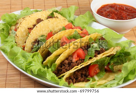 Tacos on a bed of lettuce with a bowl of salsa