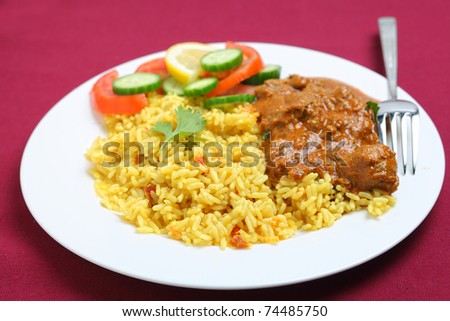 A plate of Kasmiri lamb curry with rice and salad on a maroon tablecloth.