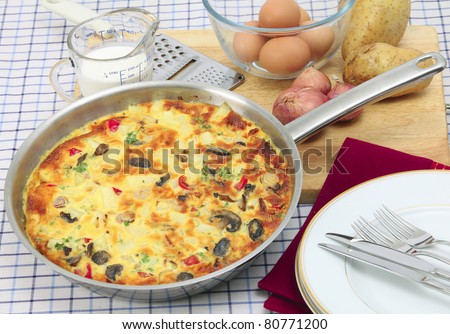 A freshly cooked Spanish omelet or tortilla de patates still in the pan, with essential ingredients behind