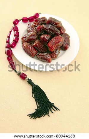 A plate of dates, eaten at fast-breaking (suhour) in Ramadan, with a string of prayer beads, on a tablecloth.