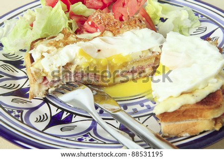 A croque madame - toasted cheese and ham sandwich topped with bechamel sauce and a fried egg - with a tomato and lettuce salad