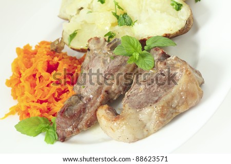 a meal of lamb loin chops with a baked potato and grated braised garlic carrots garnished with chopped parsley and sprigs of mint