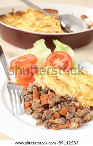 A dinner of shepherds pie or cottage pie and a salad with the serving dish in the background, vertical orientation