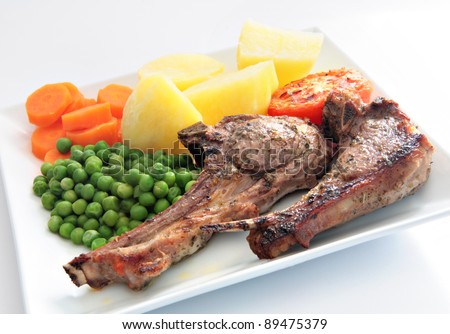A meal of grilled marinated lamb chops served with boiled potatoes, peas and carrots.