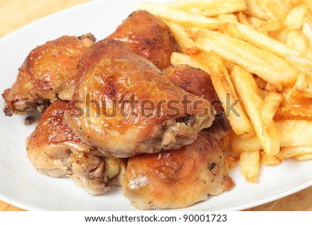 A serving dish piled with roast lemon chicken thighs and French fries, or chips