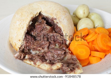 A serving plate with a steak and kidney suet pudding, boiled new potatoes and sliced carrots, a traditional English meal