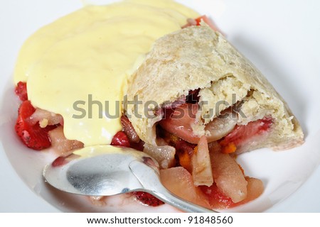 A bowl of traditional British steamed fruit pudding, of pears and strawberries with a sweet suet pastry crust, custard and an old-fashioned spoon