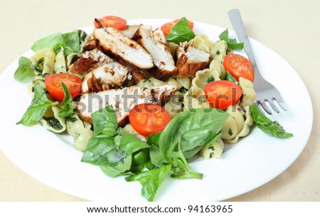 Grilled chicken breast slices served on a bed of pasta shells with spinach, garnished with tomato and fresh basil