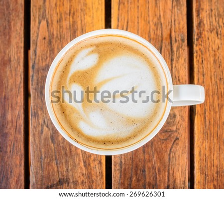 A cup of coffee with leaf pattern in a white cup on wooden background