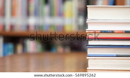 Book stack on wood desk and blurred bookshelf in the library room, education concept