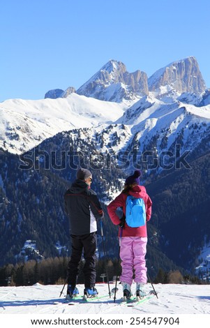 young girl in a bright track suit and a man on skis in the winter mountains in the background