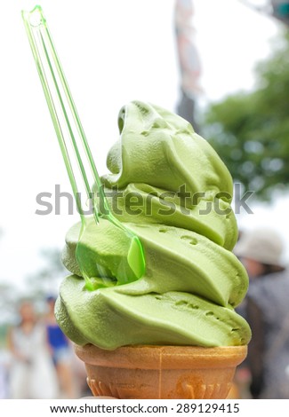 Melting Matcha Green Tea Soft Serve Cream with Plastic Spoon, Selective Focus, Blur Background. Heat and Summer Concept.