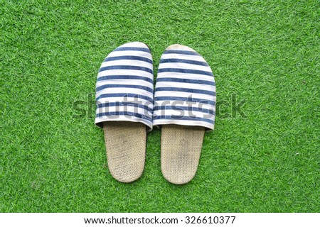 An old pair of slippers in navy blue and white stripes on artificial grass background, selective focus, relaxation concept.