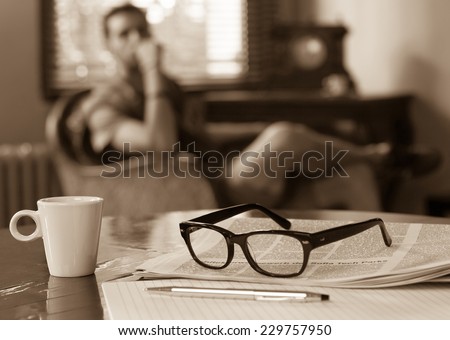 Newspapers and coffee cup, reading glasses, pen and striped paper.