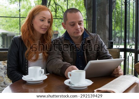 Two students drinking coffee and having fun with tablet In cafeteria