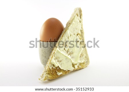 Lightly boiled egg in an egg cup with a slice of buttered toast on a white background