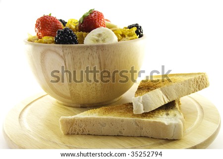 Cornflakes with strawberries, blackberries and banana in a round wooden bowl with a slice of toast on a wooden plate with a white background
