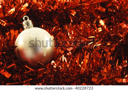Shiny silver round bauble on red tinsel background