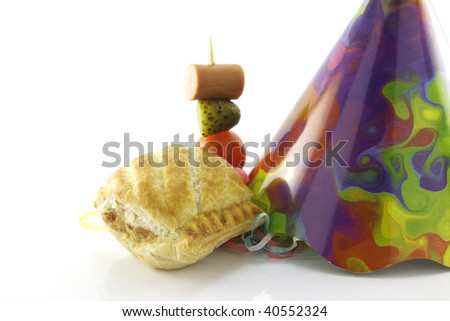 Small sausage roll with cone party hat and cocktail stick containing hot dog sausage, gherkin and tomato on a reflective white background