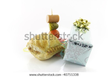 Small sausage roll with gift and cocktail stick containing hot dog sausage, gherkin and tomato with streamers on a reflective white background