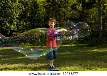 Boy makes giant bubbles outdoors on green lawn