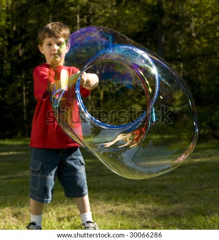 Boy makes giant bubbles outdoors on green lawn