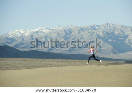 Woman runner on sand dunes with mountains.