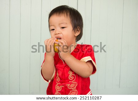 baby boy intend and tries  to eat  orange happy chinese little boy new year in Chinese style dress