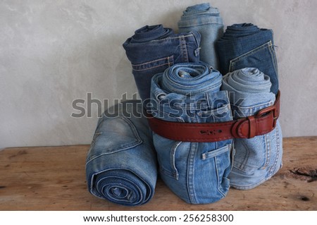 Stack roll blue denim jeans and Leather Belt on wood and concrete wall background