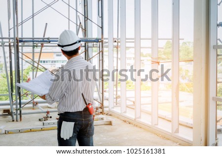 back view of smart engineer, architect or technician with white safety helmet holding blueprint in construction site building to greeting start up project, successful, business, industry concept