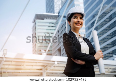 young asian business, engineer or technician woman in suit with white safety helmet looking to future and arms crossed in big city building background, business, industry and construction concept
