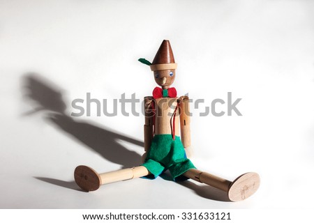 Wooden doll of Pinocchio liar with big nose and shadows on white background