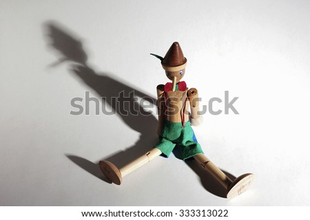 Wooden doll of Pinocchio liar with big nose. Dramatic lighting and shadows
