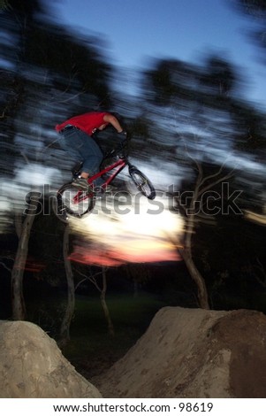 freestyle BMX rider does dirt jump with sunset as background