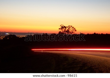 Sunset over hill with light streaks from car as forground