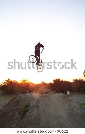 freestyle BMX rider does dirt jump with sunset as background, turndown