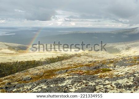 Small rainbow over severe arctic rocky plateau covered with lichens and mosses