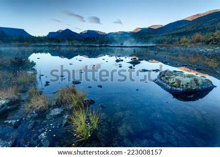 Foggy Polygonal freshwater lake with rocks and tussock in the foreground in Hibiny mountains in the early morning before sunrise