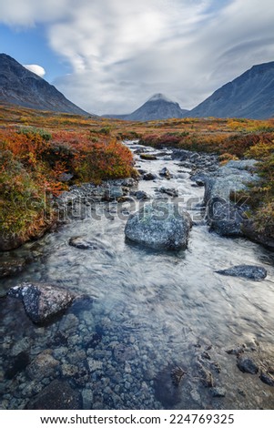 Colorful autumn tundra and mountain ridge behind the Malaya Belaya river stream in Hibiny mountains above the Arctic Circle, Russia