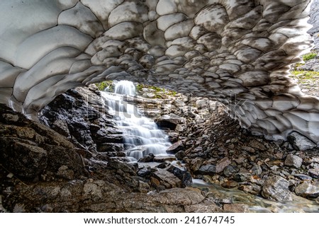 Waterfall goes under melting glacier in Hibiny mountains above the Arctic circle, Russia