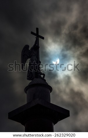 Total Solar Eclipse of March 20th, 2015 (partial phase) photographed behind a dramatic cloudy sky and an angel on top of Alexander\'s Column at Palace Square in Saint-Petersburg, Russia