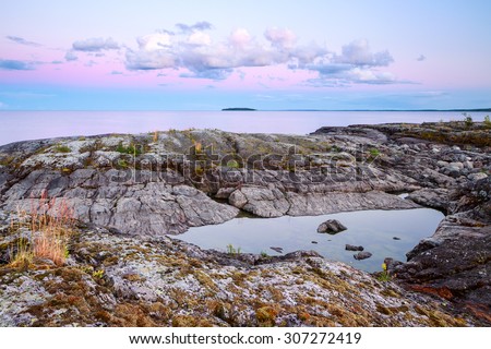 Peaceful summer sunset with subtle pink cast on cloudy sky over the island Patakansaaret in Ladoga lake, Republic of Karelia, North-West of Russia