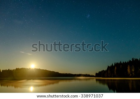 Rising moon and stars on night sky above Ladoga lake in Karelia, Russia, are reflected in still water