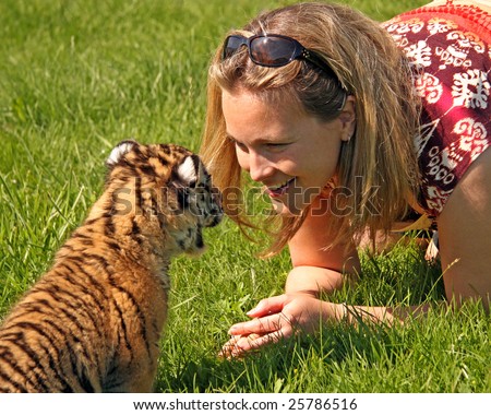 A baby tiger and a smiling pretty woman communicate nose-to-nose