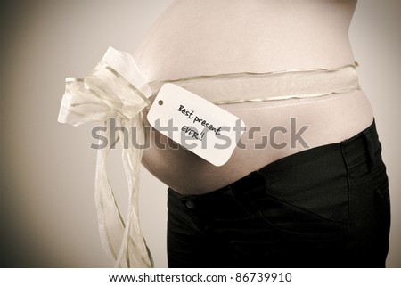 A closeup of a pregnant belly with a ribbon and a tag saying best present ever