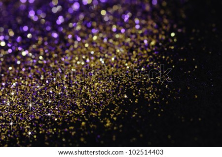 Gold and purple glitter on black background with selective focus