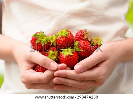 A child with several strawberries in her hands. It is summer and the photo is taken outside.
