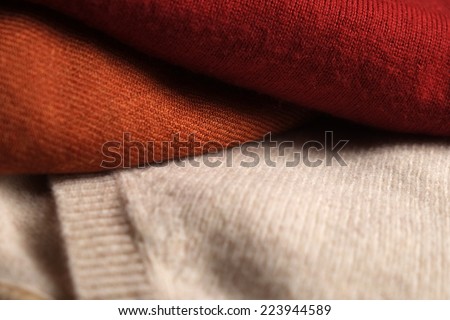 Close-up of three folded woolen sweaters. Light brown, orange and red