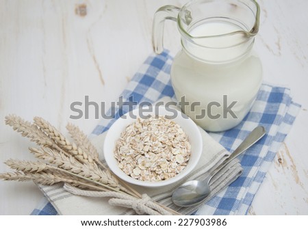Rolled oats in a white bowl on a napkin with spoon and milk on a wooden background