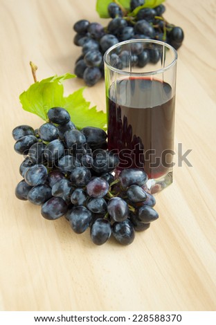 Glass of grape juice on a table with red grapes on wooden background